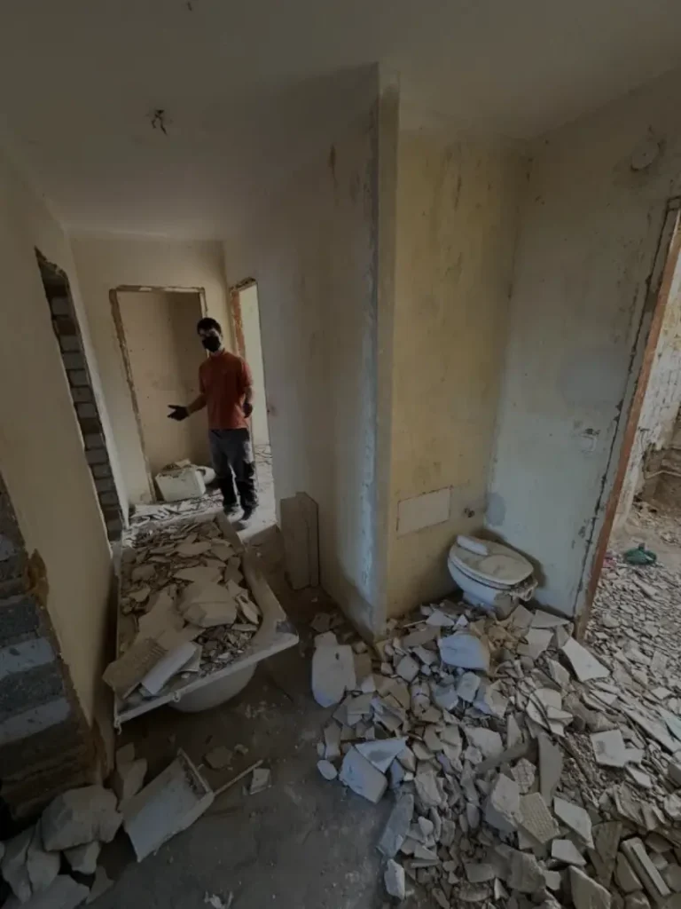 Professionelle Entkernung in Aachen: Ein Mitarbeiter von Jung und Fix steht in einem entkernten Badezimmer voller Bauschutt und Fliesenreste.